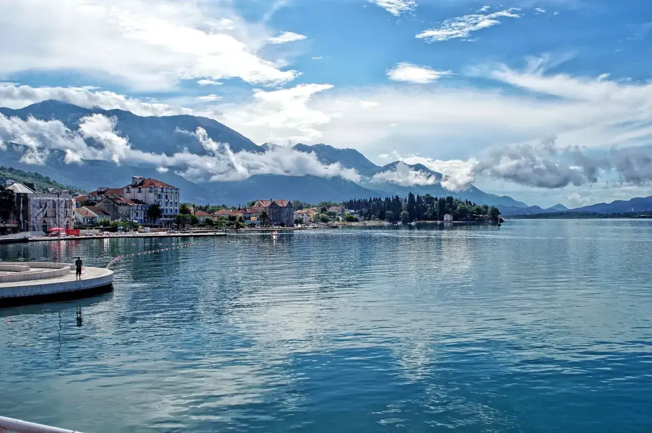 Spokojna zatoka Kotorska z górami w tle i miasteczkiem nad brzegiem.